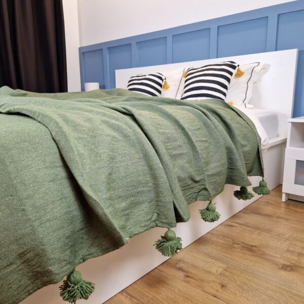 Nice modern design bedroom with blue wall paneling, olive green Moroccan pompom blanket, and zebra pillows with yellow pom poms on the bed