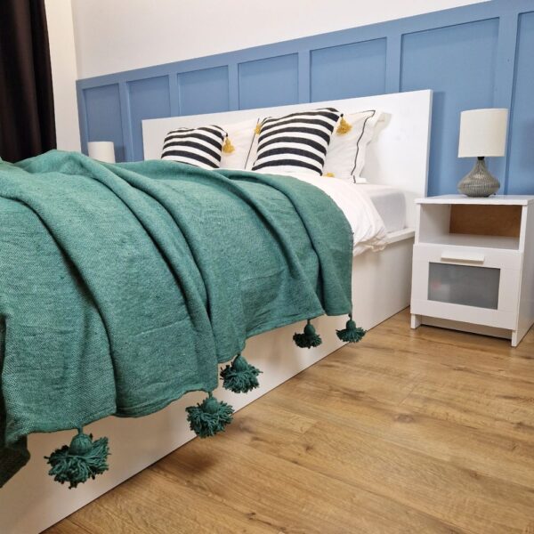 Nice modern design bedroom with blue wall paneling, dark green Moroccan pompom blanket, and zebra pillows with yellow pom poms on the bed