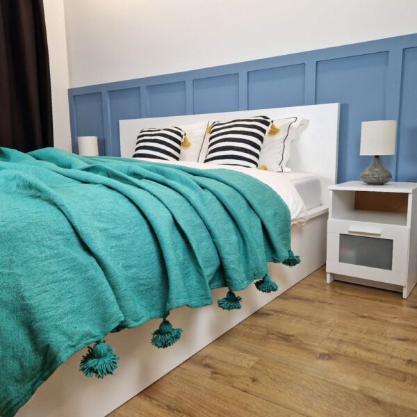 Nice modern design bedroom with blue wall paneling, green Moroccan pompom blanket, and zebra pompom pillows on the bed