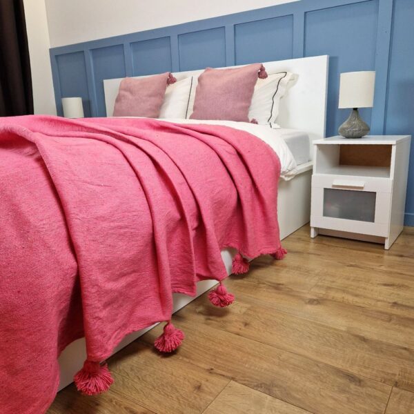 Nice modern design bedroom with blue wall paneling, Pink Moroccan pompom blanket, and Pink pompom pillows on the bed