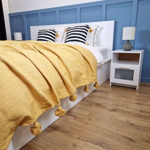 Nice modern design bedroom with blue wall paneling, mustard Moroccan pompom blanket, and zebra pompom pillows on the bed