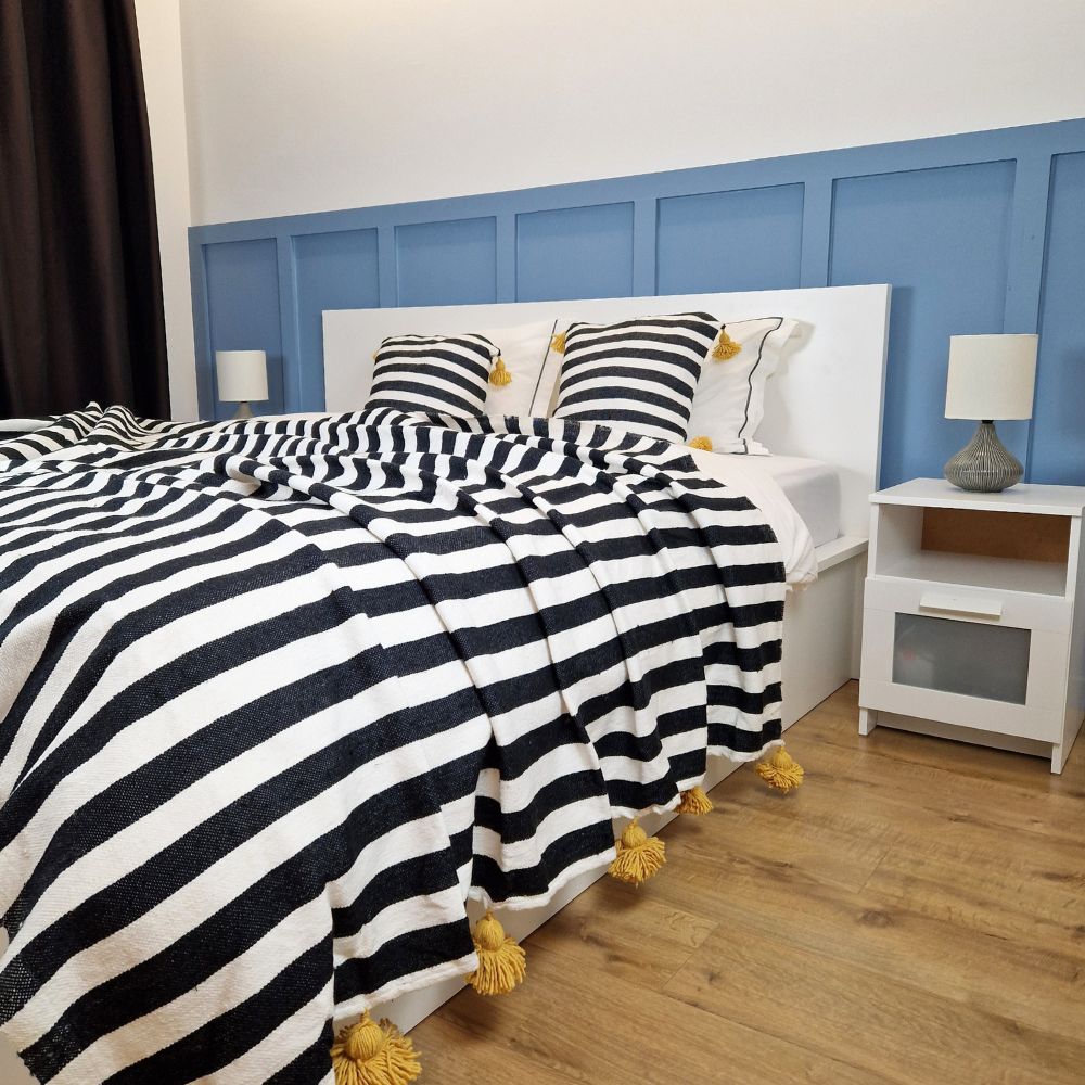 Nice modern design bedroom with blue wall paneling, black and white zebra Moroccan pompom blanket with yellow pom poms, and zebra pillows with yellow pom poms on the bed