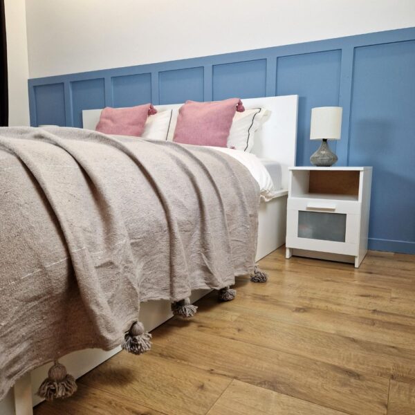 Nice modern design bedroom with blue wall paneling, Light brown Moroccan pompom blanket, and Pink pompom pillows on the bed