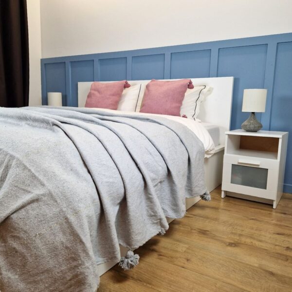 Nice modern design bedroom with blue wall paneling, Gray Moroccan pompom blanket, and Pink pompom pillows on the bed