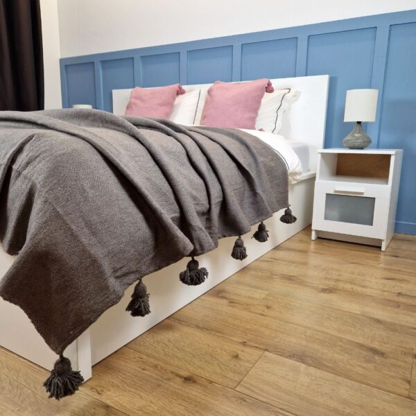 Nice modern design bedroom with blue wall paneling, Brown Moroccan pompom blanket, and Pink pompom pillows on the bed
