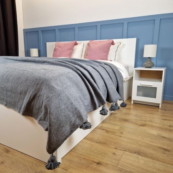 Nice modern design bedroom with blue wall paneling, Gray Moroccan pompom blanket, and Pink pompom pillows on the bed