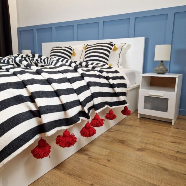 Nice modern design bedroom with blue wall paneling, black and white zebra Moroccan pompom blanket with red pom poms, and zebra pillows with yellow pom poms on the bed