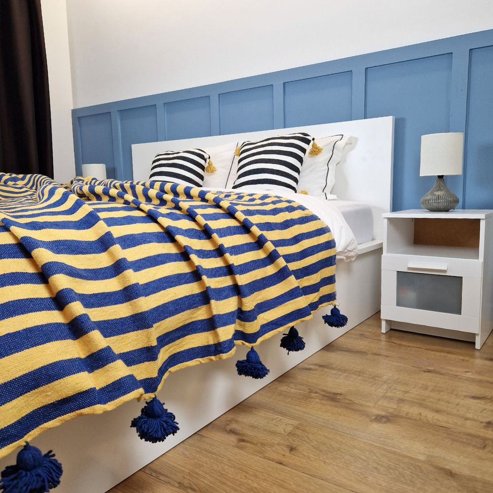 Nice modern design bedroom with blue wall paneling, yellow and blue zebra Moroccan pompom blanket with Blue stripes on the side and blue pom poms, and zebra pillows with yellow pom poms on the bed