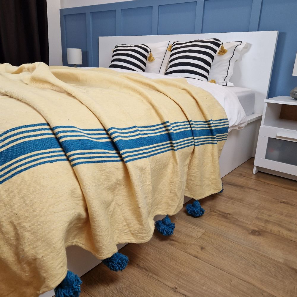 Nice modern design bedroom with blue wall paneling, yellow Moroccan pompom blanket with Blue stripes on the side and blue pom poms, and zebra pillows with yellow pom poms on the bed