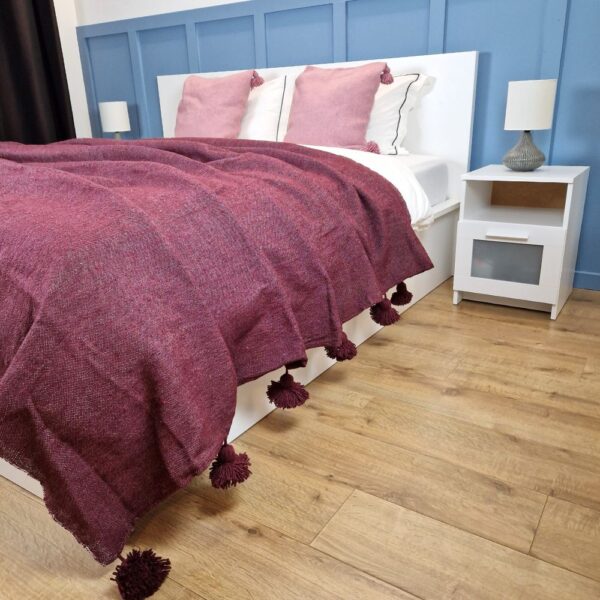 Nice modern design bedroom with blue wall paneling, Red Garnet Moroccan pompom blanket, and pink pillows with pom poms on the bed