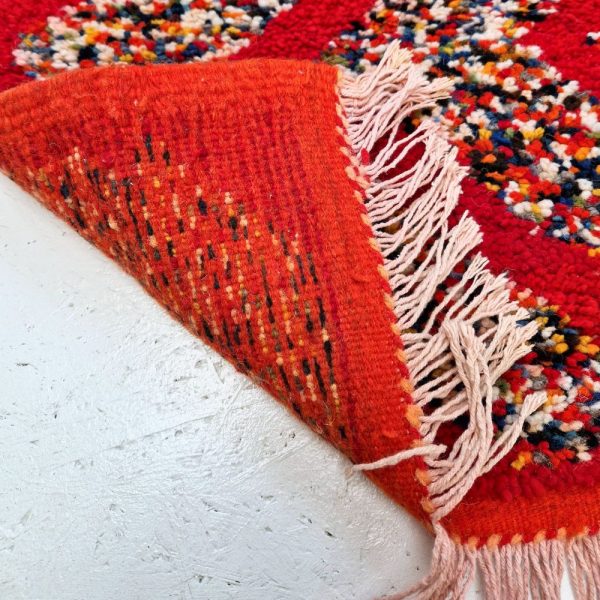 Red Moroccan rug with bold geometric patterns in white and multicolor wool, featuring abstract Berber tribal motifs and handwoven texture.