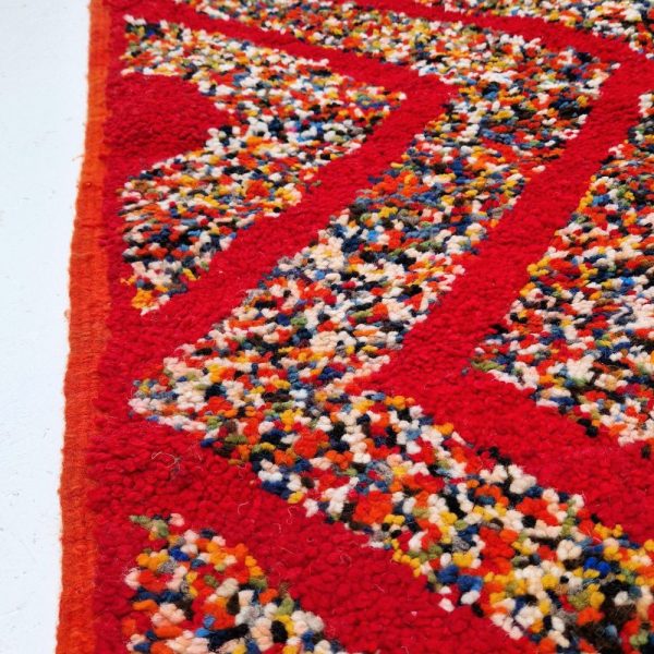 Red Moroccan rug with bold geometric patterns in white and multicolor wool, featuring abstract Berber tribal motifs and handwoven texture.