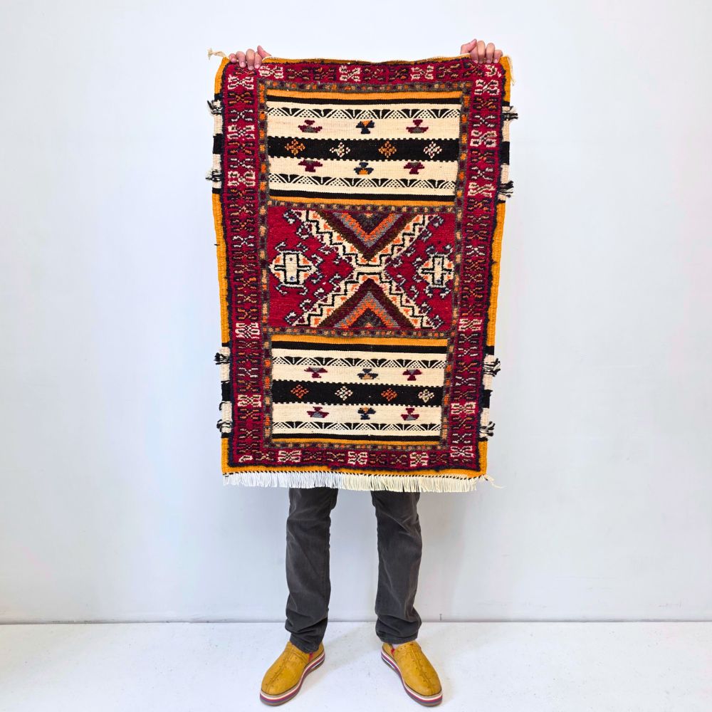 Colorful Moroccan Azilal rug with bold geometric patterns in red, orange, purple, and multicolor wool, featuring abstract Berber tribal motifs and handwoven texture.