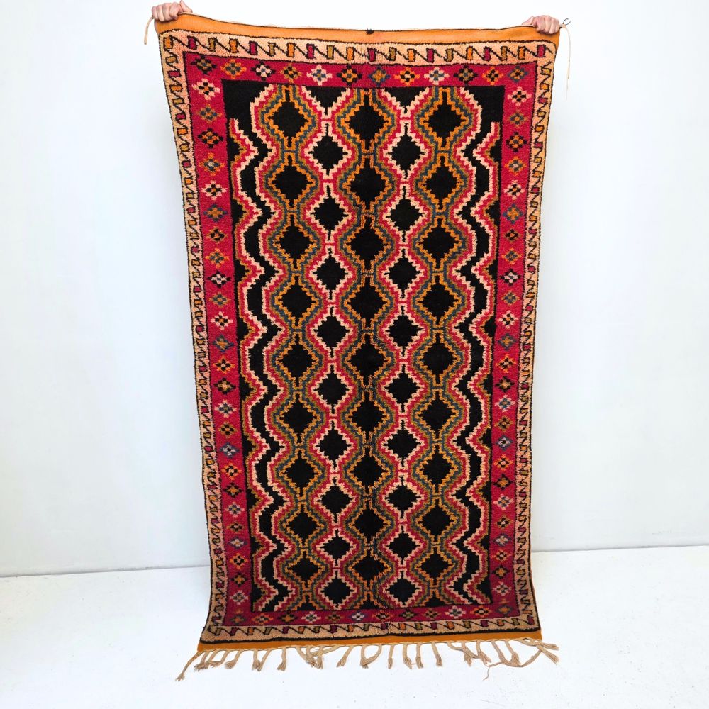 Colorful Moroccan Azilal rug with bold geometric patterns in red, orange, black and multicolor wool, featuring abstract Berber tribal motifs and handwoven texture.