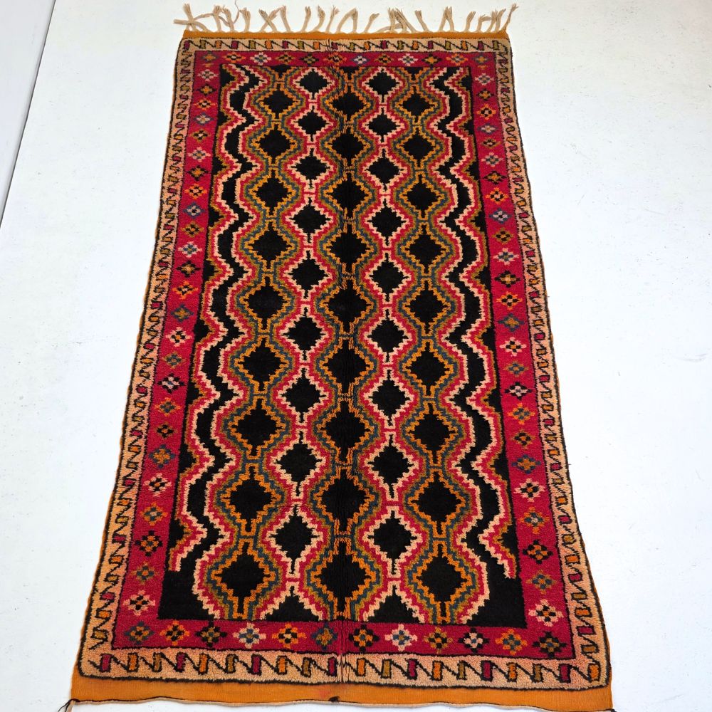 Colorful Moroccan Azilal rug with bold geometric patterns in red, orange, black and multicolor wool, featuring abstract Berber tribal motifs and handwoven texture.