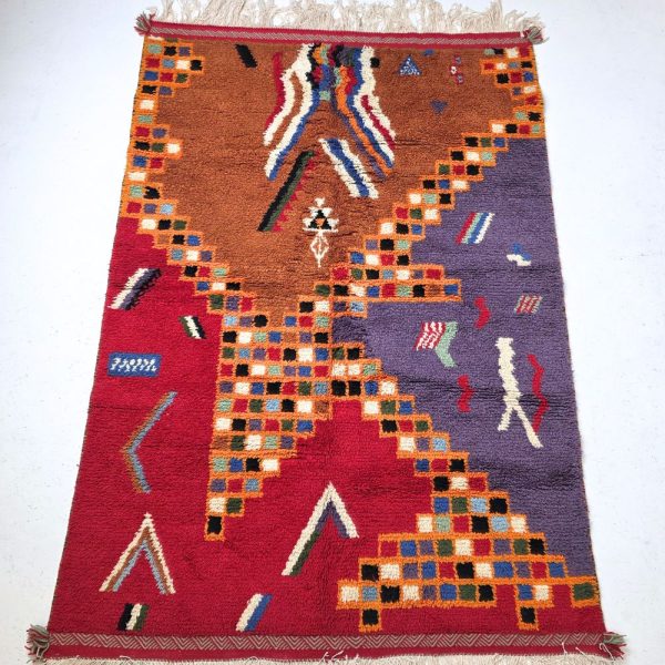 Colorful Moroccan Azilal rug with bold geometric patterns in red, orange, purple, and multicolor wool, featuring abstract Berber tribal motifs and handwoven texture.