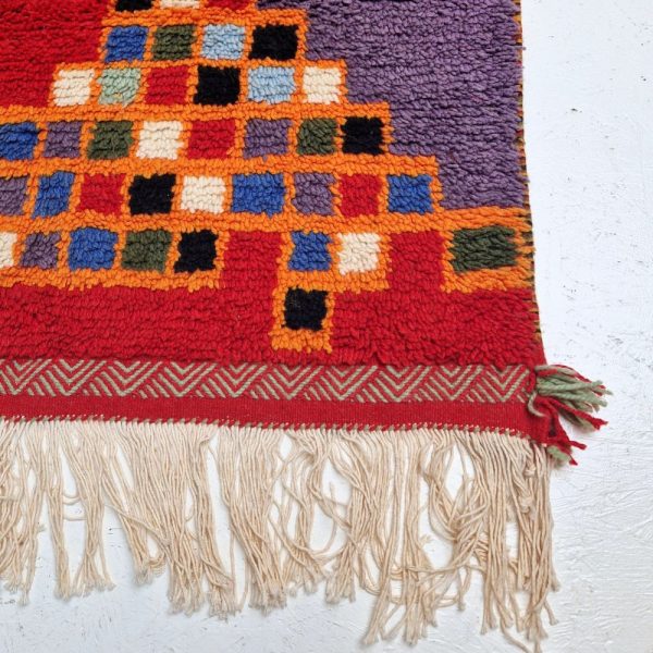 Colorful Moroccan Azilal rug with bold geometric patterns in red, orange, purple, and multicolor wool, featuring abstract Berber tribal motifs and handwoven texture.