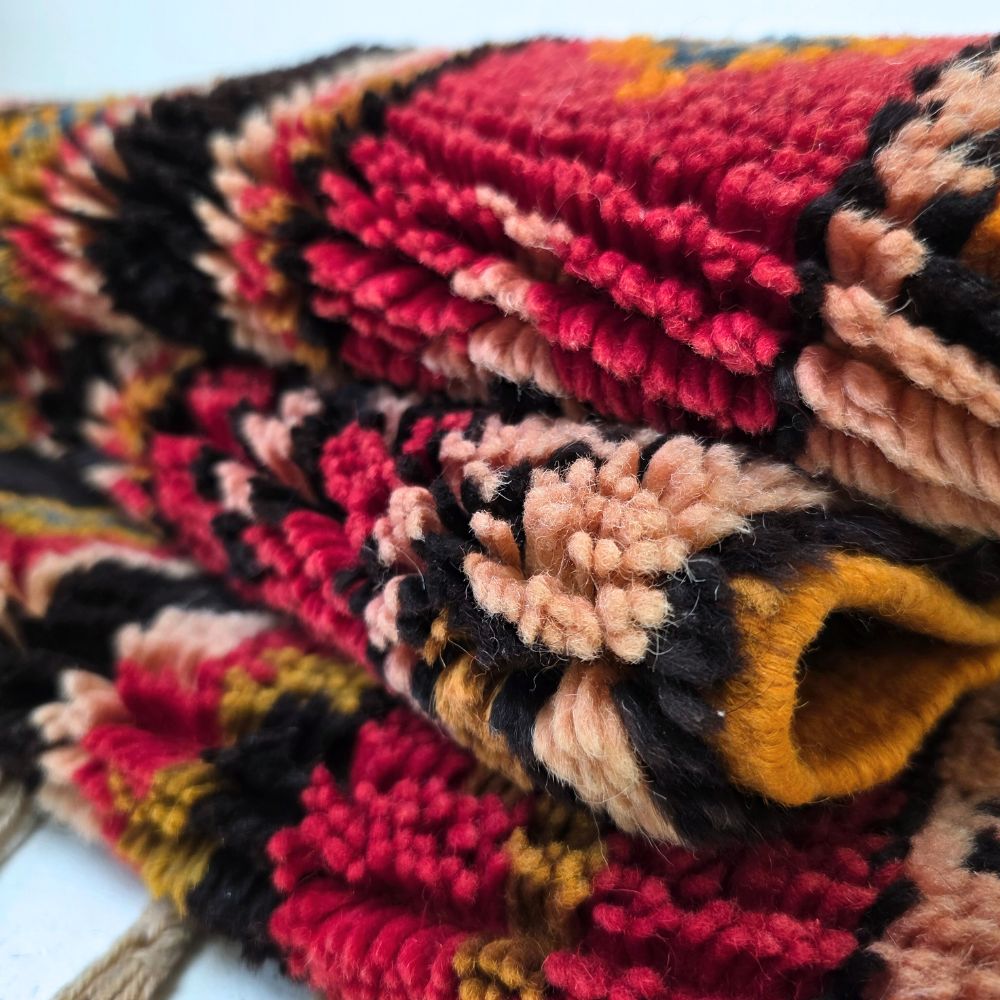 Colorful Moroccan Azilal rug with bold geometric patterns in red, orange, black and multicolor wool, featuring abstract Berber tribal motifs and handwoven texture.