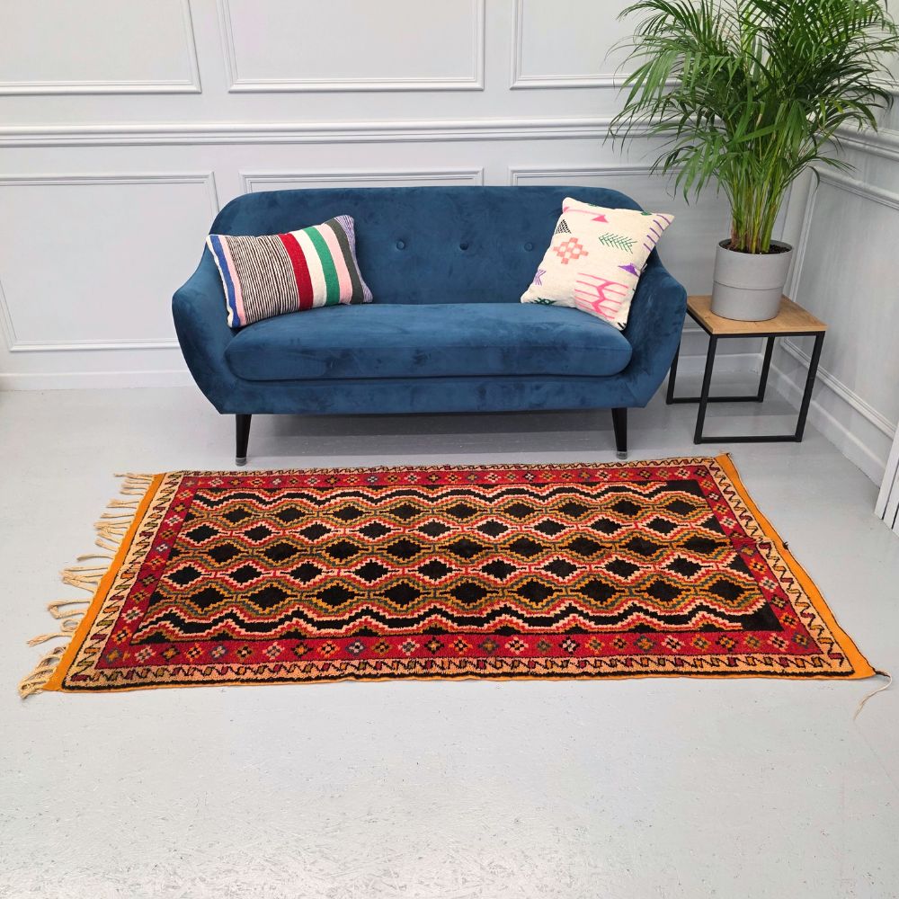 Colorful Moroccan Azilal rug with bold geometric patterns in red, orange, black and multicolor wool, featuring abstract Berber tribal motifs and handwoven texture.