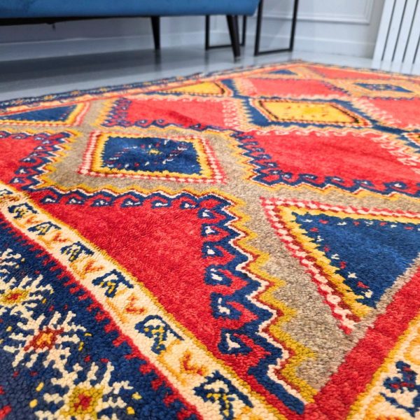 Colorful Moroccan Azilal rug with bold geometric patterns in red, orange, purple, and multicolor wool, featuring abstract Berber tribal motifs and handwoven texture.