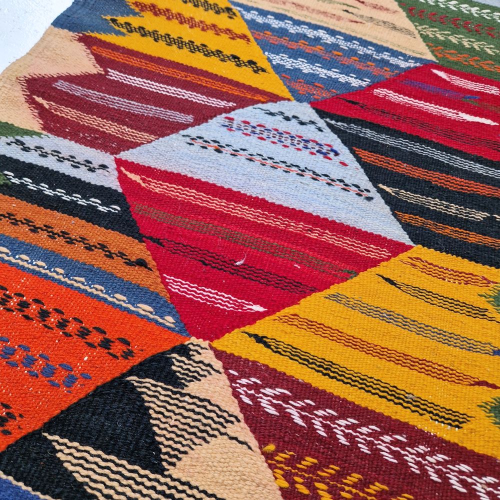 Colorful Moroccan Azilal rug with bold geometric patterns in red, orange, purple, and multicolor wool, featuring abstract Berber tribal motifs and handwoven texture.