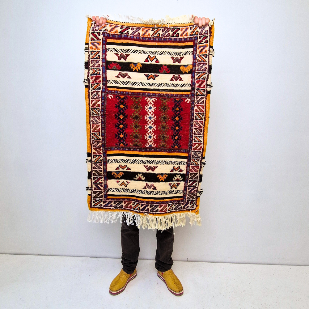 Bohemian hand-knotted rug with bold geometric patterns in red, blue, white and multicolor wool, featuring abstract Berber tribal motifs and handwoven texture.